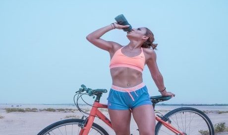 sporty woman drinking water in front of bike